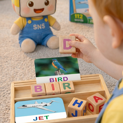 A child is holding a letter block with the letter "D" while playing with the wooden spelling blocks set that includes cards and blocks to form words like "JET" and "BIRD." A toy character is visible in the background.