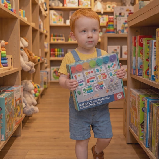 A toddler walking through a toy store while holding a colorful educational number counting toy in their hands, ready for unboxing. The toy is part of a fun, interactive math learning game designed to enhance early cognitive and motor skills in young children. The child is excited about the new toy, which is surrounded by shelves filled with more educational toys in the background.